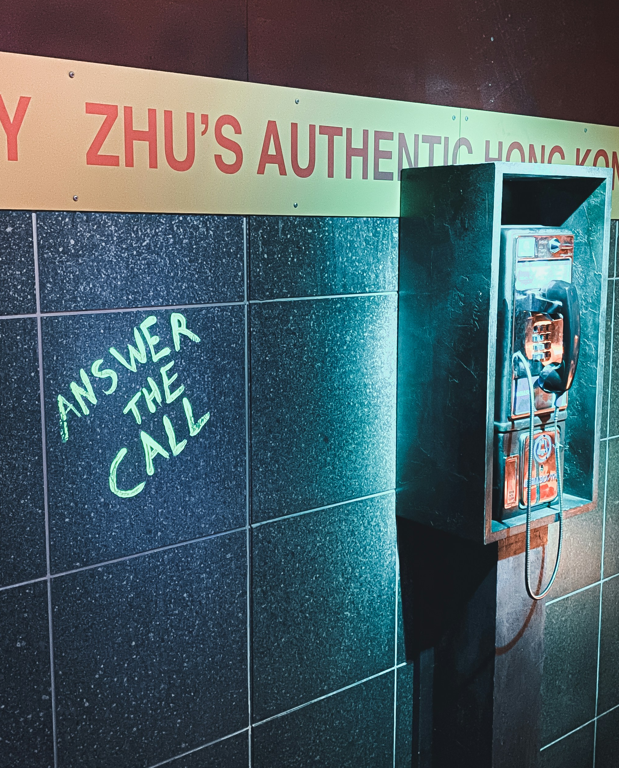 A payphone in a restaurant. Graffiti on the wall next to it says "answer the call."